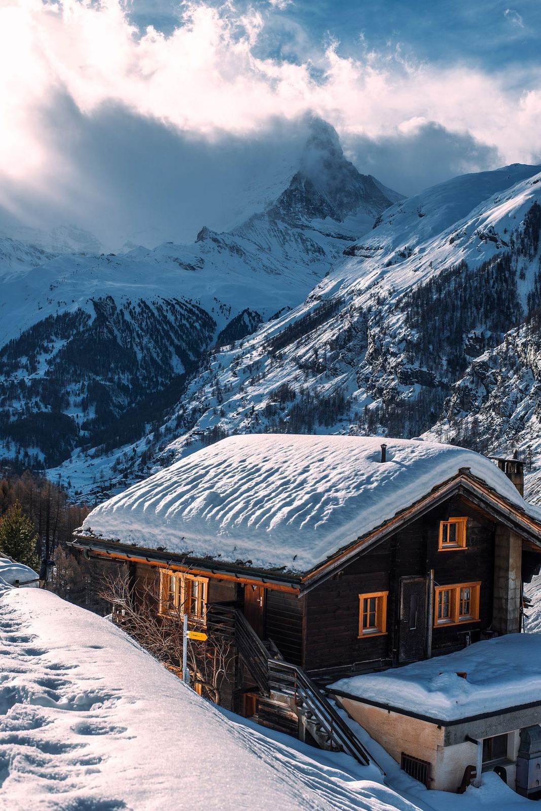 Holzchalet mit verschneitem Dach vor einem Gipfel