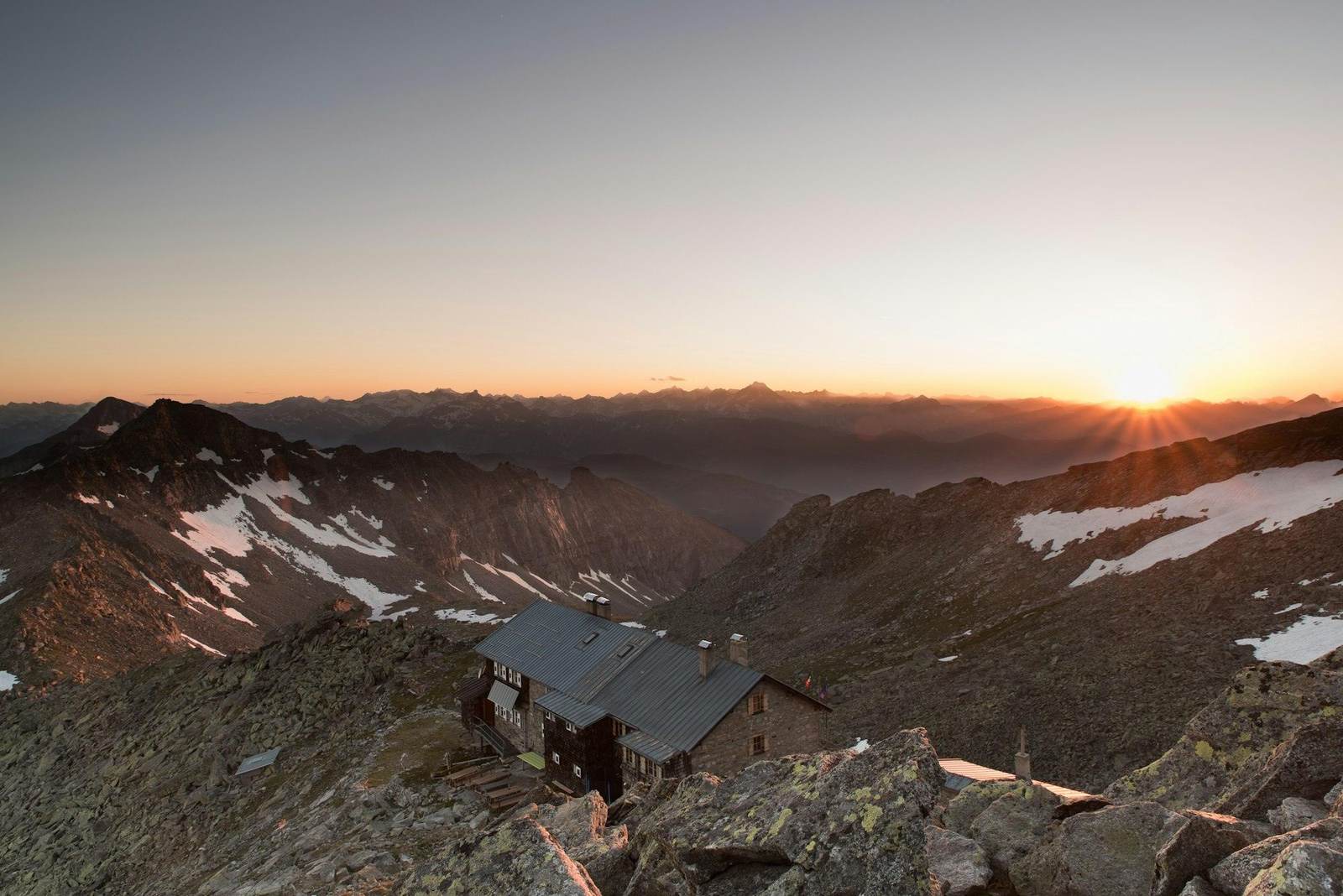 Eine Berghütte im letzten Abendlicht über den Gipfeln