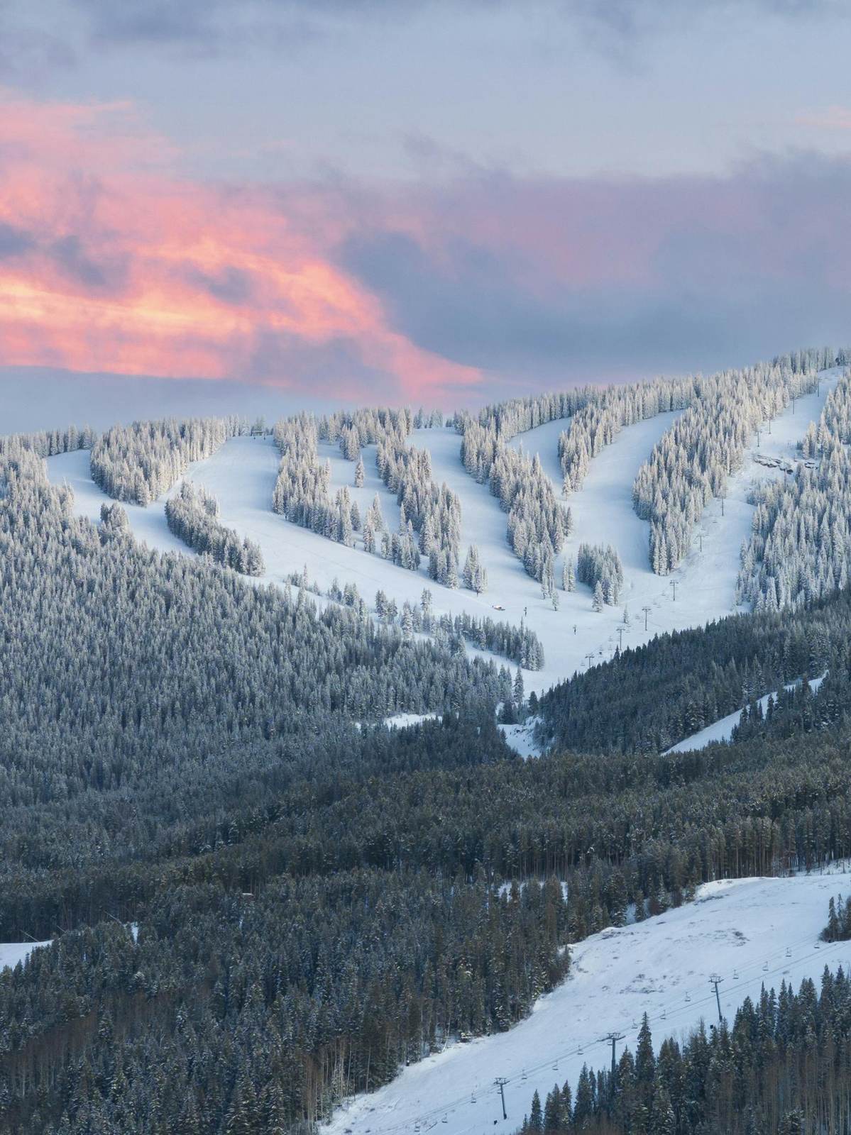 Verschneite Pisten zwischen Wald unter rosa Abendhimmel