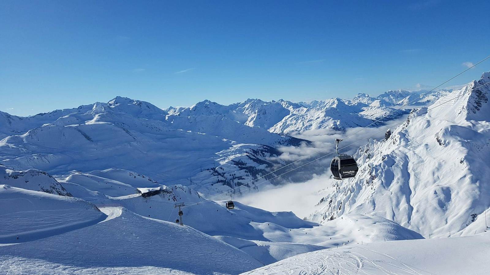 Gondelbahn über einer weiten verschneiten Berglandschaft unter blauem Himmel