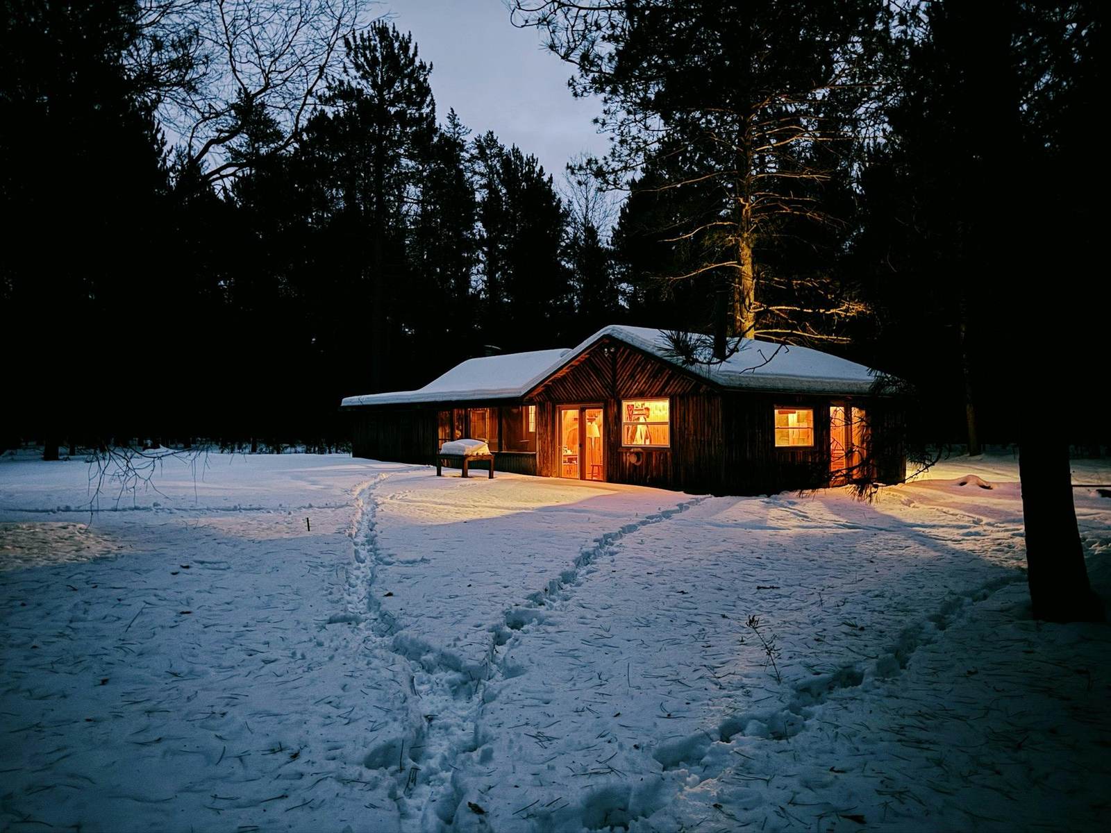 Ein beleuchtetes Holzhaus im verschneiten Wald am Abend