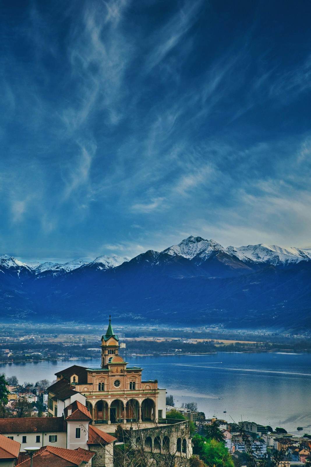 Eine Kirche über dem Lago Maggiore vor verschneiten Bergen